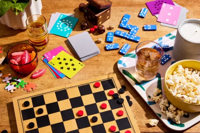 Board games, playing cards, dominoes, and snacks arranged on a table for a game night